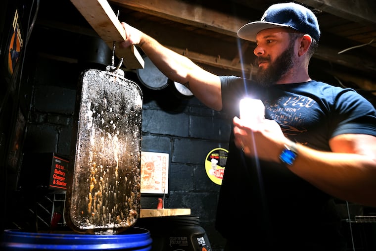 Chris Wing uses his smart phone to record video as he lifts a cast-iron pan from one of his electrolysis tanks in his basement shop in New Jersey.