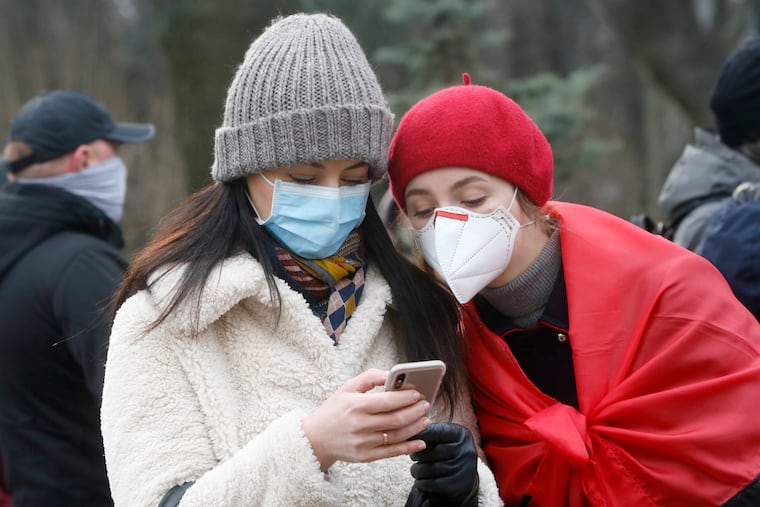 Ukrainians wearing face masks look at the latest news on a phone in Kyiv, Ukraine, Tuesday, March 17, 2020. Ukrainian authorities ruled to close public places except food markets, pharmacies and gas stations starting from Tuesday in Kyiv and other regions, and restrict the use of public transport from Kyiv to other Ukrainian cities.