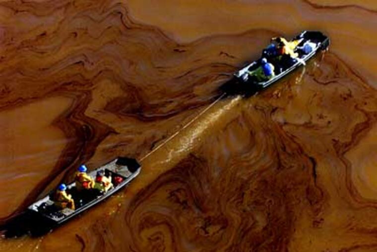 Boats carrying environmental cleanup workers pass through black oil swirled on the surface of the Delaware River after the Athos oil spill in November 2004.