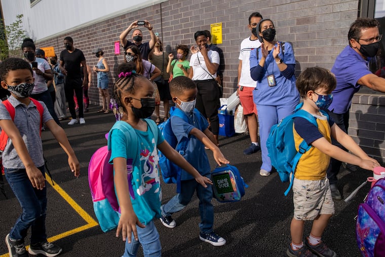 Students with arms out in front of them are attempting to keep socially distant from their classmates as they enter school on their first day of school last week.