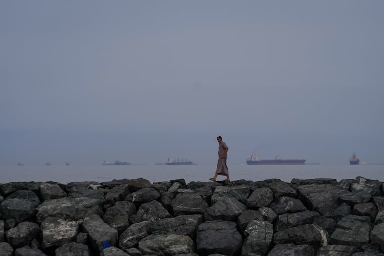 FILE - A man walks along the shore as oil tankers and cargo ships line up in the Strait of Hormuz, as seen from Khor Fakkan, United Arab Emirates, Wednesday, March 11, 2026. (AP Photo/Altaf Qadri, file)