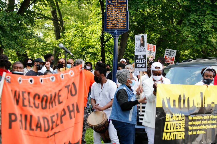 A crowd gather near a marker showing the MOVE Bombing location during a 36th anniversary remembrance march at Osage Avenue and Cobbs Creek Parkway in West Philadelphia on Thursday, May 13, 2021.