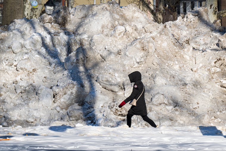 A pedestrian walks past a large pile of snow and ice along the Benjamin Franklin Parkway last week. The snowpack doesn't want to go away, it seems.
