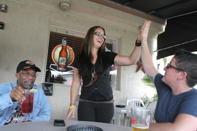 Many gay bars have disappeared in the Pennsylvania suburbs. The Beagle Tavern in Norristown has remained. It prefers to call itself a a gay-accepting bar and welcomes all. Bartender Samantha Moyer, high-fives friend and customer, Allyson Farmer, right. Jerome L. Waddles is left on the outdoor deck area on July 25, 2013. (CHARLES FOX / Staff Photographer)
