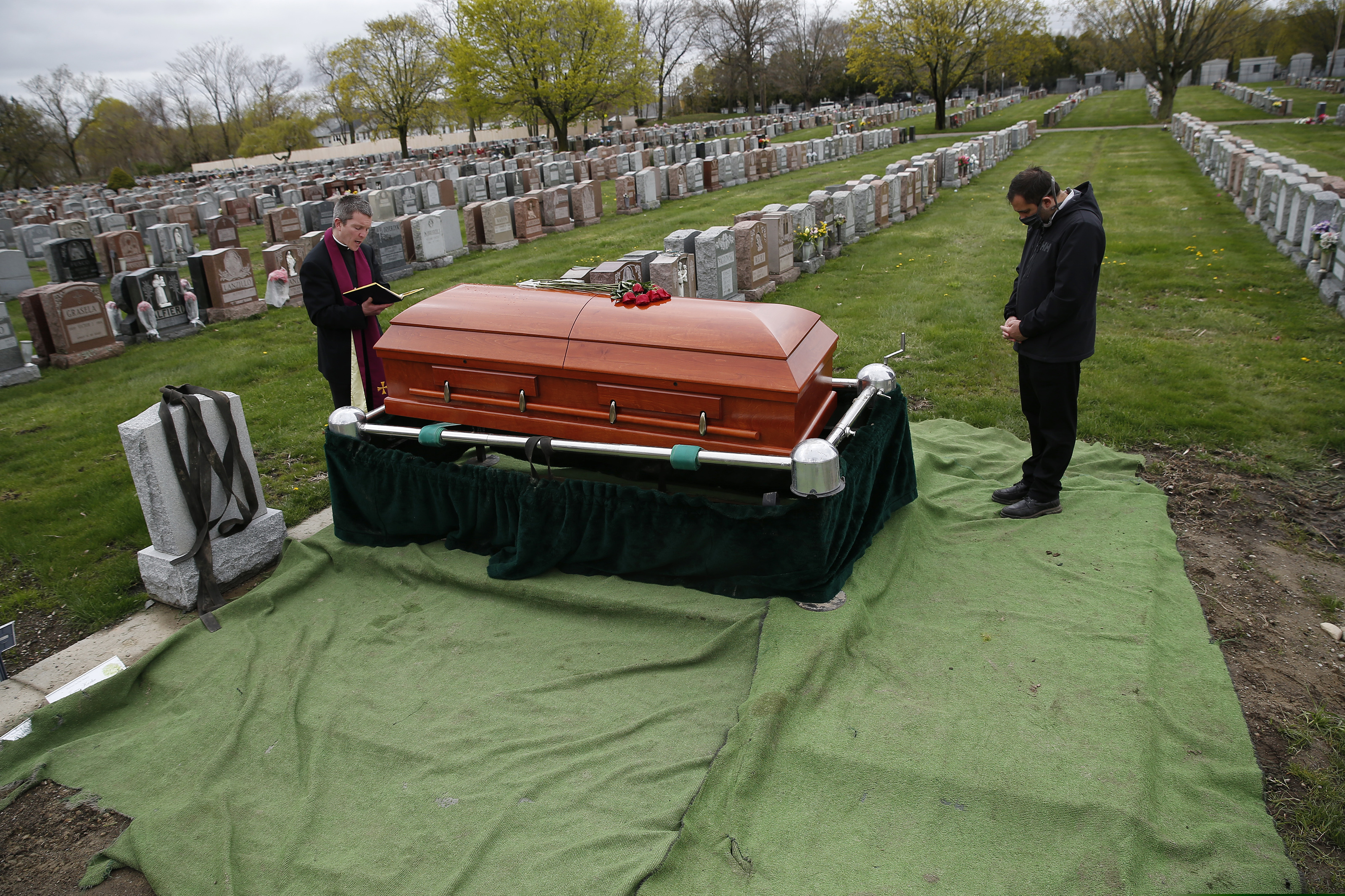 In this May 1, 2020, file photo the Rev. Eric Bennett, left, says a funeral Mass for a man who died of COVID-19 in Boston.