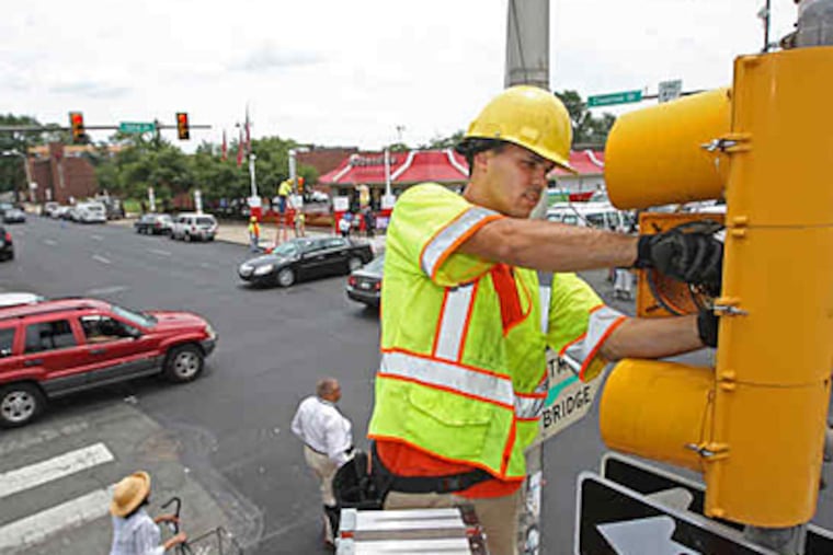 Doug Williams, a city Streets Department electrician, changes out old bulbs for LEDs in the traffic signal at 52d and Chestnut. The $6 million, six-month switchover will save energy and money.