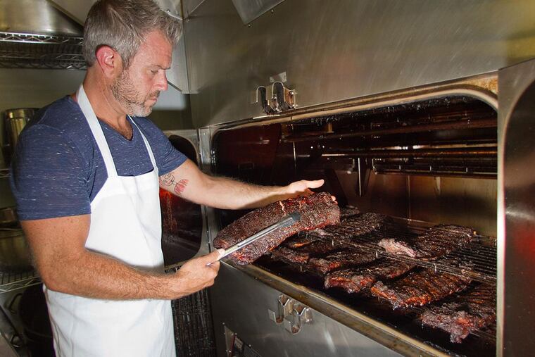 Chef-owner Chad Rosenthal checks on racks of ribs cooking in the smoker at The Lucky Well, 111 E Butler Ave, Ambler.