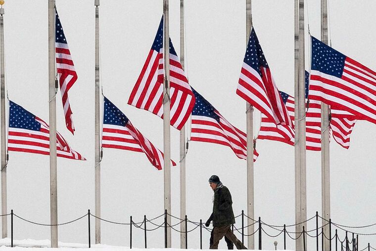 Visitors walk past flags at half-staff near the Washington Monument in Washington. Associated Press