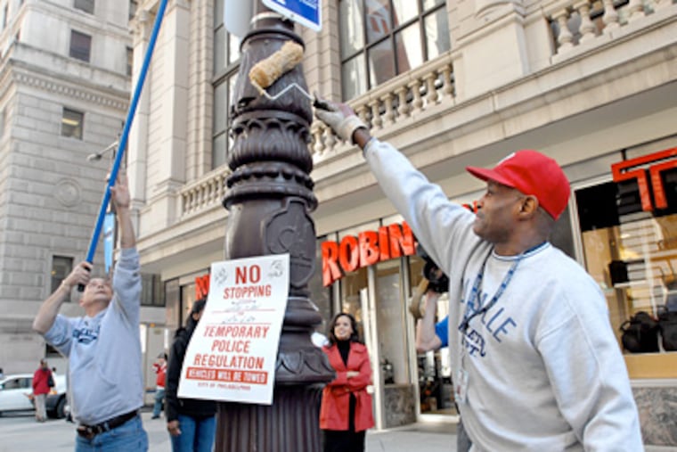 Philadelphia police officer Richard Whitford, left, and custodial worker Rufus Belton apply lubricant to a utility pole near Broad and Chestnut Streets to prevent any celebratory climbs by Phillies fans should the team win the pennant tonight. (April Saul / Staff Photographer)