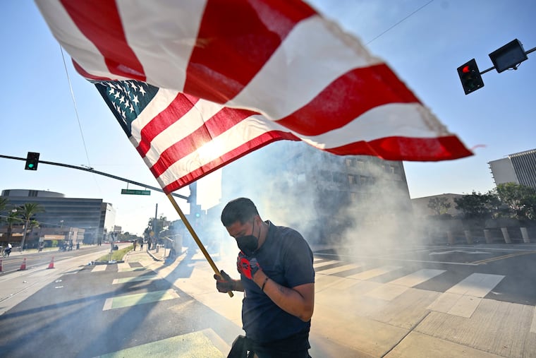 A protester raises the American flag after police use tear gas at the Federal Building in Santa Ana, Calif., on Monday.