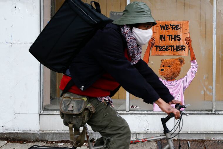 A bicyclist rides past a painting of a bear holding a sign of support during the coronavirus pandemic on the now closed Megli Furs display window in South Philadelphia on Monday, April 27, 2020.