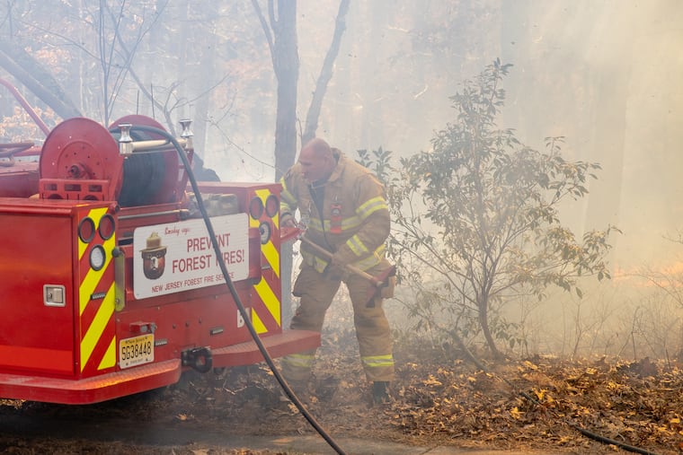 Firefighters work the scene of a brush fire in Medford, NJ, Mar. 14, 2021. A resident reported that the wind picked up embers from a fire pit and spread the fire. High winds and dry conditions sparked brush fires around the state creating a challenge for crews who struggled to contain the blazes.