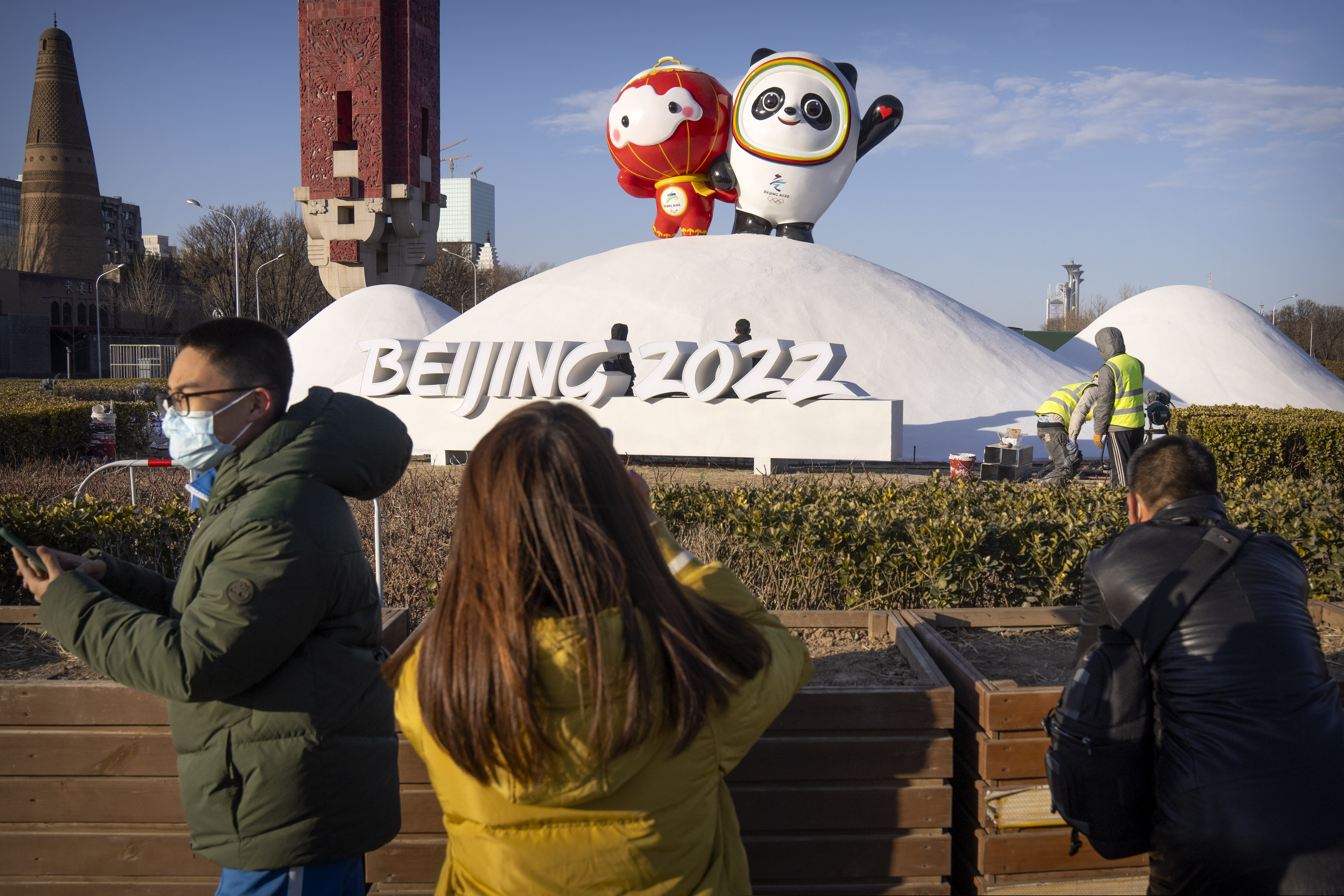 People wearing face masks to help protect against the coronavirus look at a display of the Winter Paralympic mascot Shuey Rhon Rhon (left) and Winter Olympic mascot Bing Dwen Dwen near the Olympic Green in Beijing.