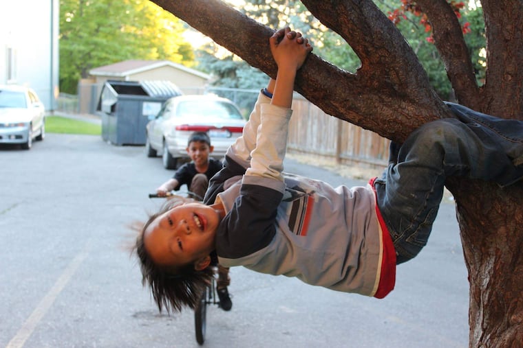 Peh Reh, 9, a refugee from Burma, hangs on a tree while Prabin Biswa, 8, originally from a Bhutanese refugee camp, rides his bike nearby on June 13, 2013. This photo was taken near Quincy Apartments in Twin Falls, Idaho, where the author's family first resettled.