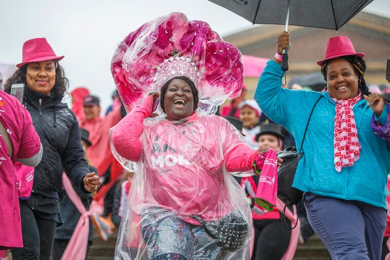 Joy Briggs (center) of Darby, came to the walk wearing a large pink carnival-style headpiece, but due to the weather she had to wrap it in plastic to protect it. She celebrates surviving cancer with Ameera Ali (lef) of Wilmington, Del., and Tawanda Johnson (right) of Camden on the steps of the Art Museum on Sunday.
