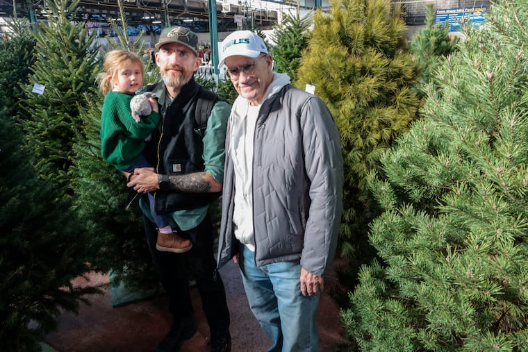 Bob Nark (right) with son Jason holding 3-year-old daughter Penelope among Christmas trees at the Pennsylvania Farm Show in Harrisburg, Thursday, January 9, 2025.