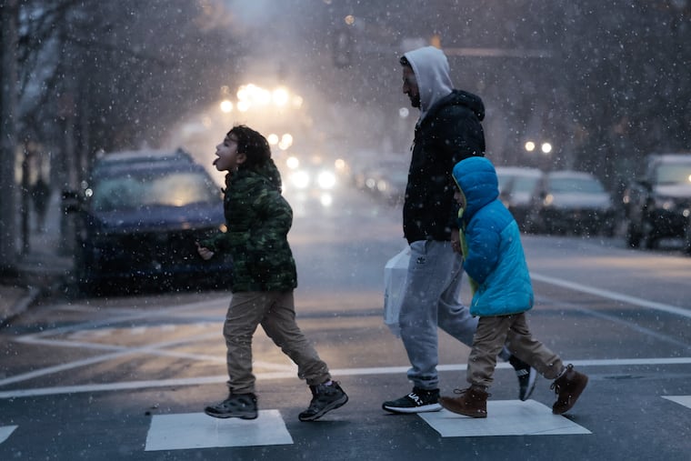 A young person tries to catch some snow on their tongue while crossing Walnut Street at 45th Street in West Philadelphia on Friday.
