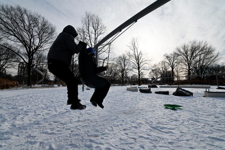 Jason Chestnut (left) rides a swing with his son Caleb, 10, at the snow-filled Anna C. Verna Playground at FDR Park in South Philadelphia after a paltry snowfall last month. They've all been pretty paltry so far.