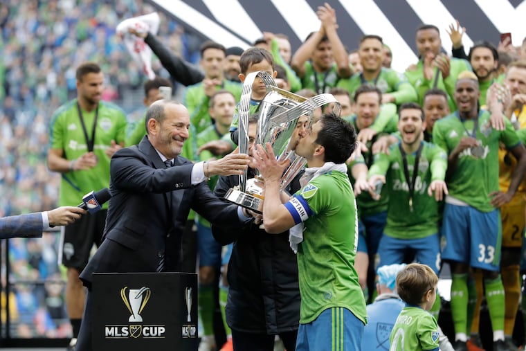 Seattle Sounders midfielder and captain Nicolás Lodeiro (right) kisses the MLS Cup trophy after receiving it from commissioner Don Garber.