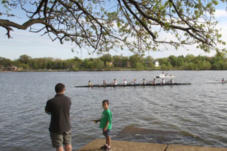 A young boy fishes while crew teams practice on the Cooper River at Cooper River Park in 2012. ( Charles Fox / Staff Photographer )