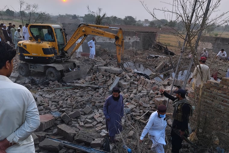 A worker clears rubble with an excavator as a police officer and local residents gather at the site of an overnight suicide bombing at a security post in Fatah Khel, in Bannu, a district in Pakistan's Khyber Pakhtunkhwa province bordering Afghanistan, Sunday, May 10, 2026.