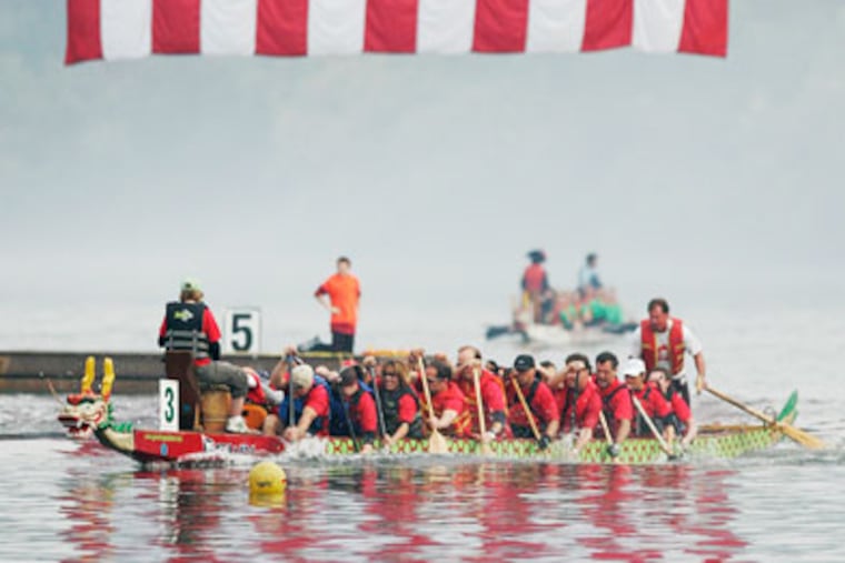 Dragon boat #3 Wyeth Wyverns paddle down the Schuylkill river in the 10th race of the morning. The huge American flag that was hanging fromthe Strawberry Mansion Bridge was reflected in the river. ( Michael Bryant / Staff Photographer )