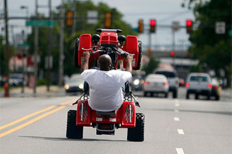 ATV rider, Mook, who didn't want to give his real name, wheelies down Lehigh Avenue on a recent Sunday ride. Mook is a member of Philly Hang Gang. Operating an ATV or dirt bike is illegal in Philadelphia. (David Maialetti / Staff Photographer)