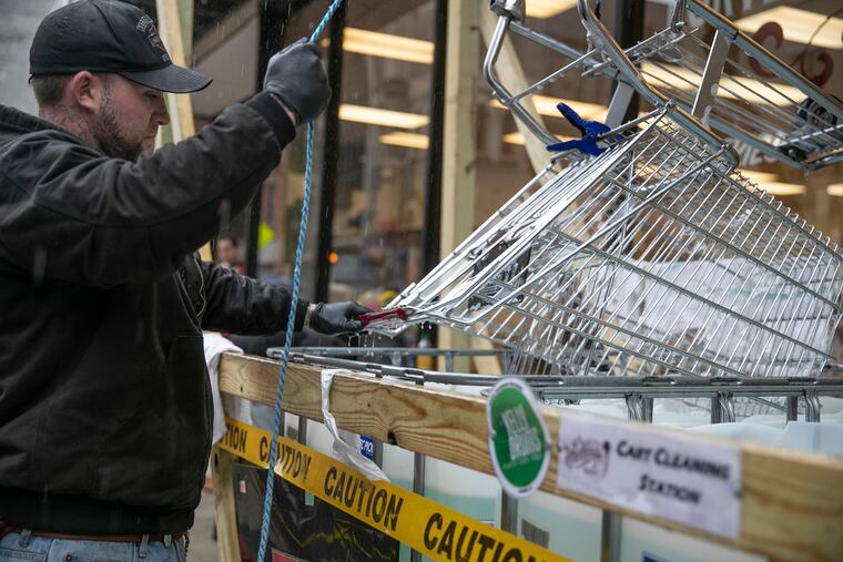 Sean Cooper puts a grocery cart into a disinfectant dunk station set up by Rittenhouse Market at 17th and Spruce in Philadelphia on Saturday, March 28, 2020. Carts are disinfected every time a customer uses one. The market is implementing this precaution due to the spread of the coronavirus.