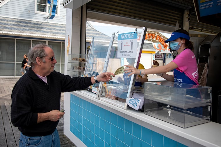 Andy Weiner, of Haddonfield, N.J., owner of Splash Zone Water Park, orders a chocolate frozen custard from Kiera O’Mallui, 17, of Northeast Philadelphia, at Kohr Bros Frozen Custard along the Wildwood boardwalk at Wildwood, N.J., on Saturday, May 23, 2020. Food businesses have employees wearing masks and a plastic screen to prevent the spread of coronavirus.