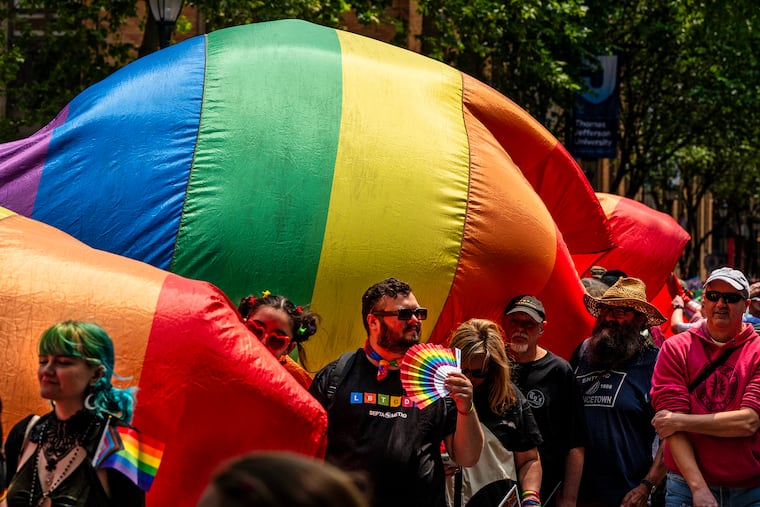 Marchers carry one of the sections of the progress pride rainbow flag up Walnut Street.