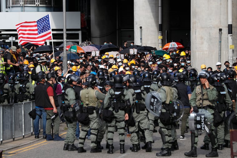 Protesters hoist a U.S. flag as they face off with riot police at the entrance to a village at Yuen Long district in Hong Kong Saturday, July 27, 2019. Thousands of protesters began marching Saturday despite police warnings that their presence would spark confrontations with local residents. Demonstrators wearing black streamed through Yuen Long, the area where a mob brutally attacked people in a commuter rail station last Sunday.