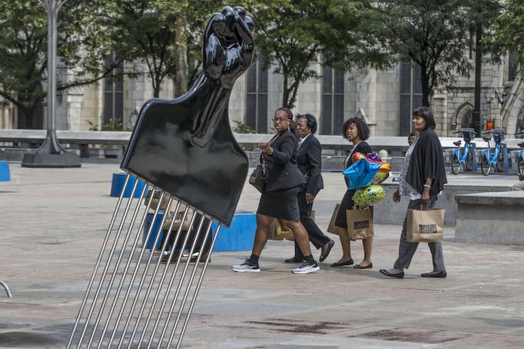 Pedestrians walk across Thomas Paine Plaza across from City Hall on Tuesday, Sept.12, 2017, and notice the new piece of art, “All Power to All People," by Hank Willis Thomas.