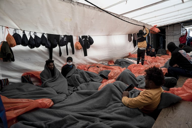 Migrants wrapped in blankets and waterproof bags lie on the deck of the Ocean Viking rescue ship, in the Strait of Sicily, in the Mediterranean Sea, Saturday, Nov. 5, 2022.