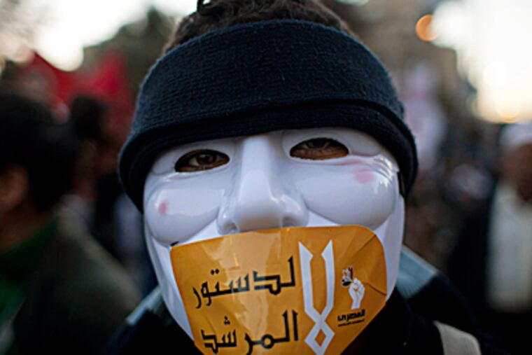 An Egyptian protester with a mask on his face and a sticker with Arabic that reads "No for the constitution of the Morshid," during an anti-president Mohammed Morsi protest near the presidential palace, in Cairo on Friday. Egypt's political crisis spiraled deeper into bitterness and recrimination Friday as thousands of Islamist backers of the president vowed vengeance at a funeral for men killed in bloody clashes earlier this week and large crowds of the president's opponents marched on his palace to increase pressure after he rejected their demands. NASSER NASSER / Associated Press