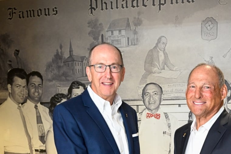 Tim Abell, president (left), and Richard Green, chairman, of Firstrust Bank, in front of a mural at the company's Ridge Pike headquarters near Conshohocken. The mural depicts Green's father and grandfather, who built the bank, with earlier employees.
