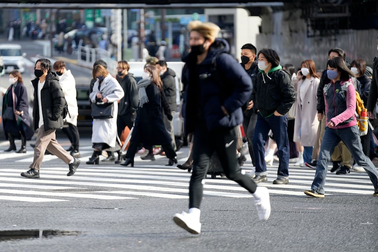 People wearing face masks walk along a pedestrian crossing at Shibuya in Tokyo.