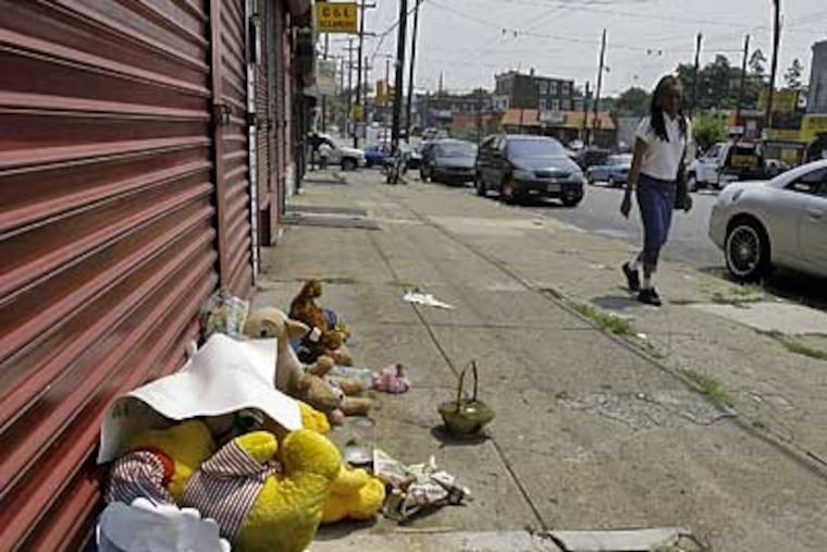 Someone walks past a make-shift shrine in front of the Urban Wear on Wyoming Ave. where Amissi Ndikumasab was shot. (Akira Suwa / Inquirer)