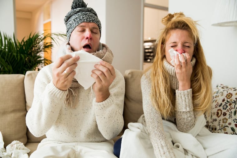 A couple sneezing and sick from the flu at home.