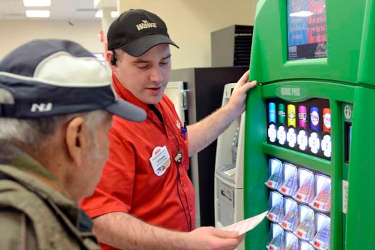 Wawa assistant general manager Stephen Rooney (right) helps a customer (he did not want this name used) with using the new NJ Lottery vending machine in the Wawa on Haddonfield Road in Cherry Hill November 22, 2013. The Lottery partnership with Wawa is being rolled out and currently about 30 NJ Wawa stores out of 240 have the freestanding machines. ( TOM GRALISH / Staff Photographer )