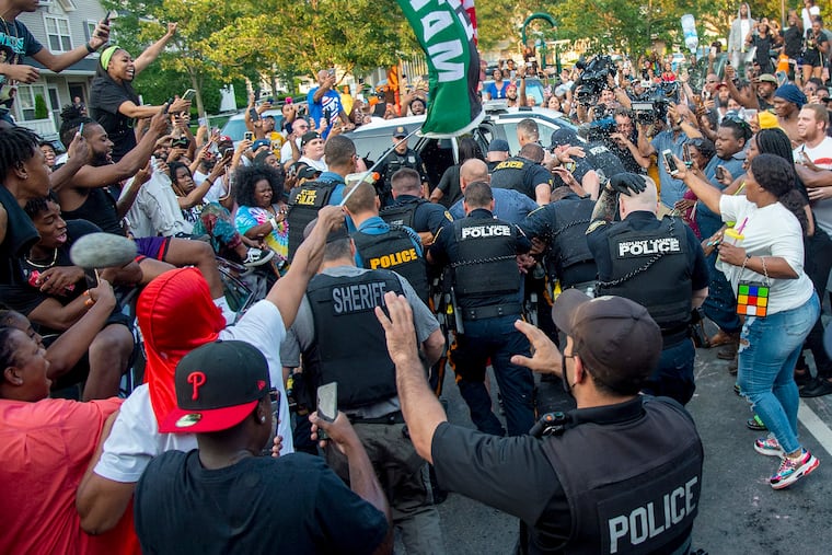 Police escort Edward Cagney Mathews through a crowd of people who had gathered outside his Mount Laurel home, Monday, July 5, 2021. Mathews, a white man who is being called racist after a video went viral of him pushing a Black neighbor with his chest and using racist slurs to address the neighbor and others, was arrested Monday after protesters gathered at his home for hours.