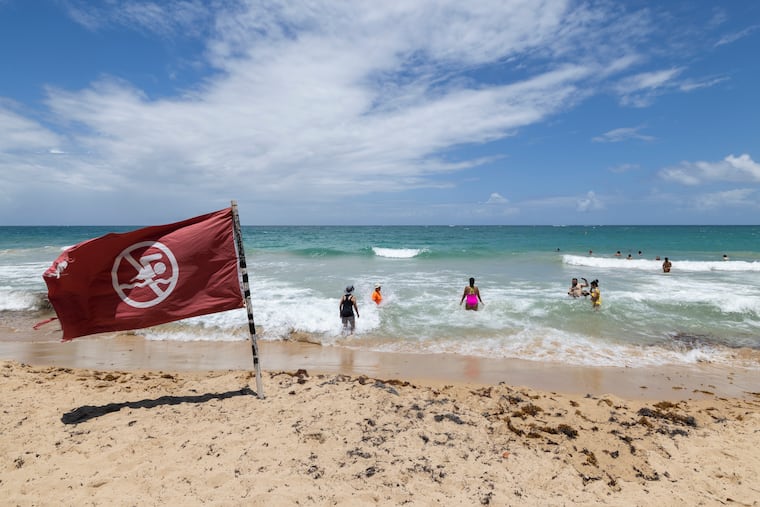 A warning flag flies on the beach as people swim in Condado, Puerto Rico, as Hurricane Erin approaches, Friday, Aug. 15, 2025. (AP Photo/Alejandro Granadillo)