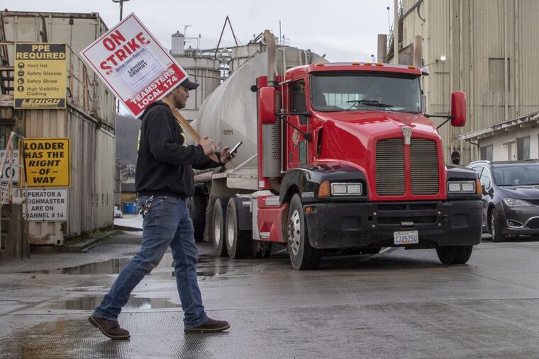 Adam Meader, a silo operator with Lehigh Cement, left, and Ric Hornibrook, a mixer truck driver with Cadman Concrete, block a truck loaded with raw cement powder used to make concrete for two minutes as the truck driver waits to head out of the plant in Seattle on Friday, Jan. 14, 2022. Both men are members of Local #174. The driver of the truck is an independent contractor. Striking workers are allowed to block trucks entering and exiting the plant for two minutes. The strike has halted some construction projects across the region. (Ellen M. Banner/The Seattle TImes/TNS)