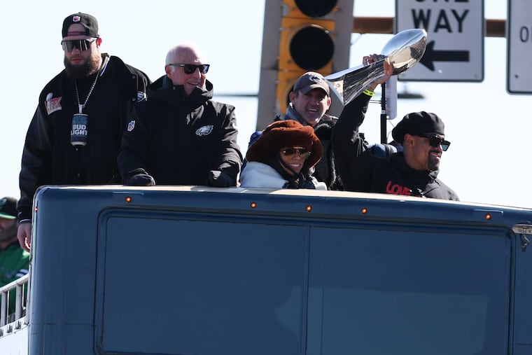 Eagles quarterback Jalen Hurts waves the Lombardi Trophy as he, team owner Jeffrey Lurie, and others ride on a bus during the Super Bowl LIX victory parade in February.