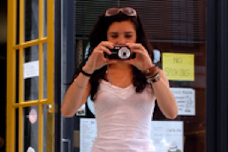 Restaurant patron Melissa Pugh of Gloucester takes a picture of fellow customer Bobaji as he's seated in the sidecar of owner Van Frederick's motorcycle outside Cafe Ole in Old City.