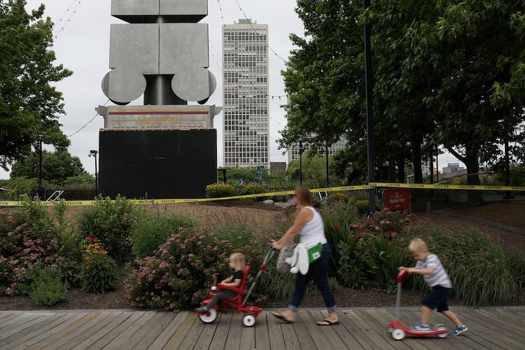 A woman and children pass by the boarded-up Christopher Columbus monument at Penn’s Landing in Philadelphia on Wednesday, June 17, 2020. The Delaware River Waterfront Corporation , which maintains the monument, is covering up the bottom of the obelisk until the end of a public feedback process to determine whether it should be removed.