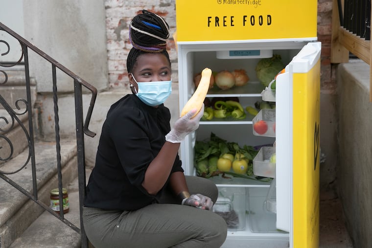 Michelle Nelson, founder of Mama-Tee, shows off a squash that was donated while she restocks the Community Fridge outside of Ambassador restaurant in the Ludlow neighborhood of Philadelphia on Saturday.