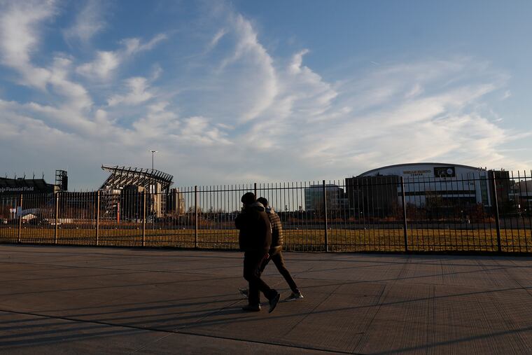 Pedestrians walk along the sidewalk on Pattison Avenue in South Philadelphia with the Wells Fargo Center and Lincoln Financial Field in the background on Sunday, December 19, 2021.