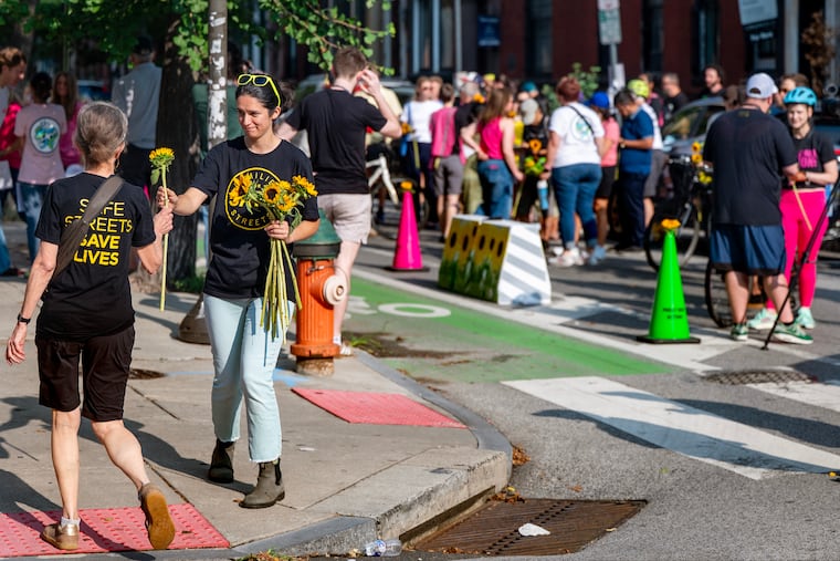 Hanna Kahler hands out sunflowers as family, friends, and Philly Bike Action members arrive at the angel bike for Barbara Friedes at 18th and Spruce Streets for a memorial Sunday, July 19, 2026. Friedes, a 30-year-old Children's Hospital of Philadelphia doctor, was killed on her bike by a drunk driver in July 2024.