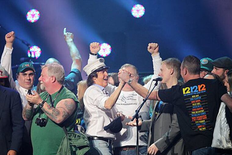 This image released by Starpix shows Paul McCartney, center, on stage with firefighters at the 12-12-12 The Concert for Sandy Relief at Madison Square Garden in New York on Wednesday, Dec. 12, 2012. Proceeds from the show will be distributed through the Robin Hood Foundation. (AP Photo/Starpix, Dave Allocca)