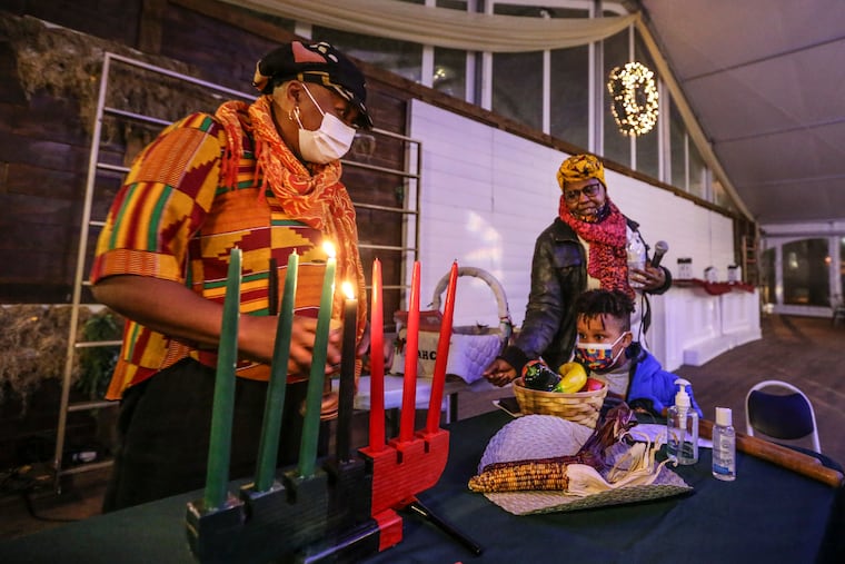 Karen Smith (left) lights the kinara together with Phoenix Mystique and James Eckenrode, 4, on the second night of Kwanzaa and gives thanks at Franklin Square with the African American Museum in Philadelphia in December 2021.